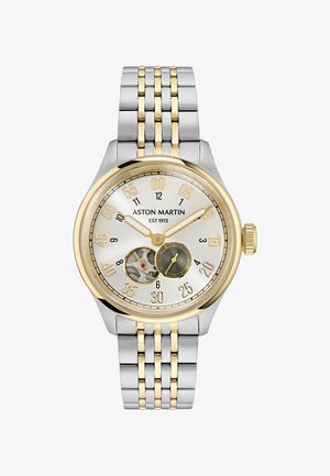 Strieborné a zlaté náramkové hodinky Aston Martin s viditeľnými mechanizmami, zlatými hodinovými a minútovými ručičkami a nerezovým a zlatým náramkom.