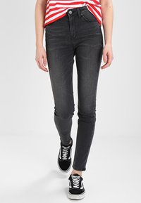 Svarta skinny jeans med hög midja, tillverkade av denim, med dragkedja och knappstängning, kombinerade med svarta sneakers och en rödrandig topp.