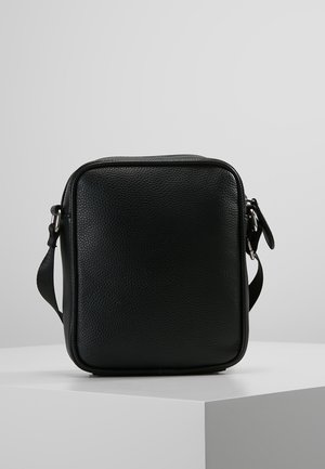 Borsa a tracolla in pelle nera testurizzata con tracolla regolabile, forma rettangolare e chiusura con zip, esposta su una superficie bianca con sfondo grigio.