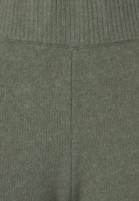 Olivgrüner Strickstoff mit einem gerippten Bund und einer weichen, strukturierten Oberfläche. Nahtdetails sind in der Mitte sichtbar.