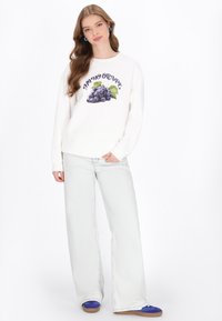 Hanorac alb cu grafică de strugure și text, asortat cu blugi evazați de culoare bleu deschis și pantofi albaștri. Material neted cu croială lejeră.