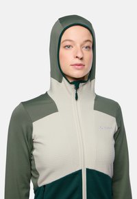 Grüne und cremefarbene Zip-Jacke mit Kapuze, ausgestattet mit strukturiertem Material, einem mehrfarbigen Design und einem gestickten Logo auf der Brust.
