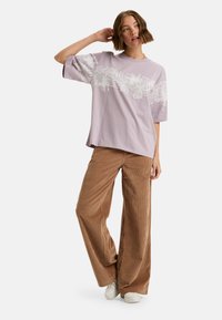 Lavendel katoenen t-shirt met witte bloemenborduring, brede korte mouwen, gecombineerd met een bruine corduroy wijde broek en witte sneakers.