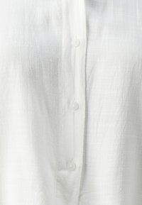 Camicia bianca con bottoni, realizzata in tessuto testurizzato, caratterizzata da una fila di bottoni in plastica discreti lungo il centro anteriore.