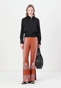 Svart knapp-up skjorte, rustfargede bukser med bred ben og hvite motiver, samt svarte slingback sandaler; parret med en stor svart tote-veske.