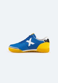 Zapatilla de lona azul con logo X blanco, contrafuerte amarillo y suela texturizada. Presenta cordones azules y forro blanco.