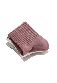 Trois paires de chaussettes côtelées pliées en rose pâle, blanc et gris clair empilées sur un fond blanc.
