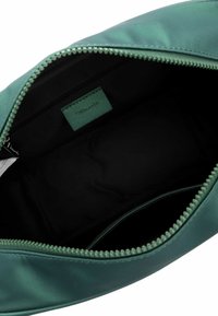 Grøn stofpose med en glat, mat finish. Har en toplynlås, en indvendig lomme og et mærke. Indersiden er sort og rummelig.