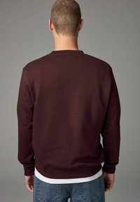 Sudadera burdeos de tela suave, con cuello redondo y mangas largas, con una camisa blanca de capas debajo.