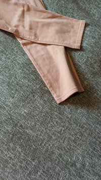 Béžové bavlněné kalhoty položené na strukturovaném šedém povrchu, které ukazují design rovného střihu a upravený lem bez dalších detailů či vzorů.