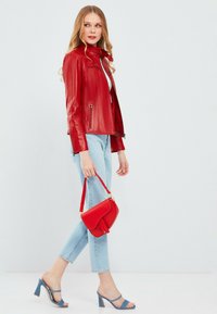 Rode leren jas met ritszakken, gecombineerd met lichtblauwe cropped jeans. Gedeeltelijk gedragen met blauwe hoge sandaalhakken en een kleine rode handtas.