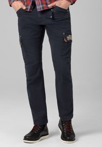 Navy cargo pants made from durable fabric feature multiple pockets, textured accents, and a tapered fit, paired with black boots and red laces.