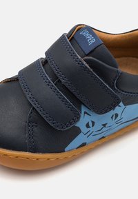 Marineblaue Lederschuhe mit zwei Klettverschlüssen, verfügen über ein blaues Katzendesign an der Seite, ein weiches Innenfutter und eine braune Gummisohle.