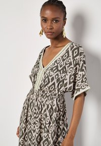 Geprinte jurk in groen en beige, met een V-halsontwerp, elastische tailleband en versierd kant langs de halslijn en mouwen.