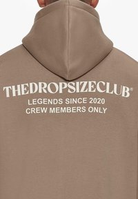 Brown hoodie featuring a large white graphic text on the back that reads "THEDROPSIZECLUB LEGENDS SINCE 2020 CREW MEMBERS ONLY."
