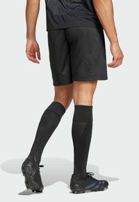 Pantalones cortos deportivos negros con un acabado texturizado y suave, combinados con calcetines negros hasta la rodilla y botas negras con un diseño elegante y tachuelas.
