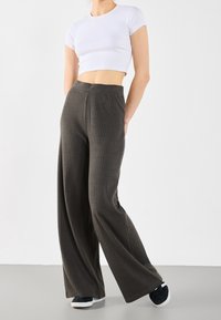 Weite, gerippte, dunkelgraue Hose mit elastischem Bund, kombiniert mit einem enganliegenden weißen Cropped-Top und schwarzen Sneakers. Glatte Textur, lässiges Design.