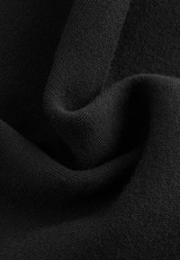 Gros plan d’un tissu noir doux avec une texture tricotée visible et des plis doux créant des ombres et des reflets.