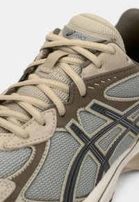 Αθλητικά παπούτσια με μπεζ διχτυωτό επάνω μέρος, καφέ σουέτ λεπτομέρειες και μαύρες λεπτομέρειες. Διαθέτουν χοντρές κορδόνες και υφασμάτινη σόλα από ελαστικό.