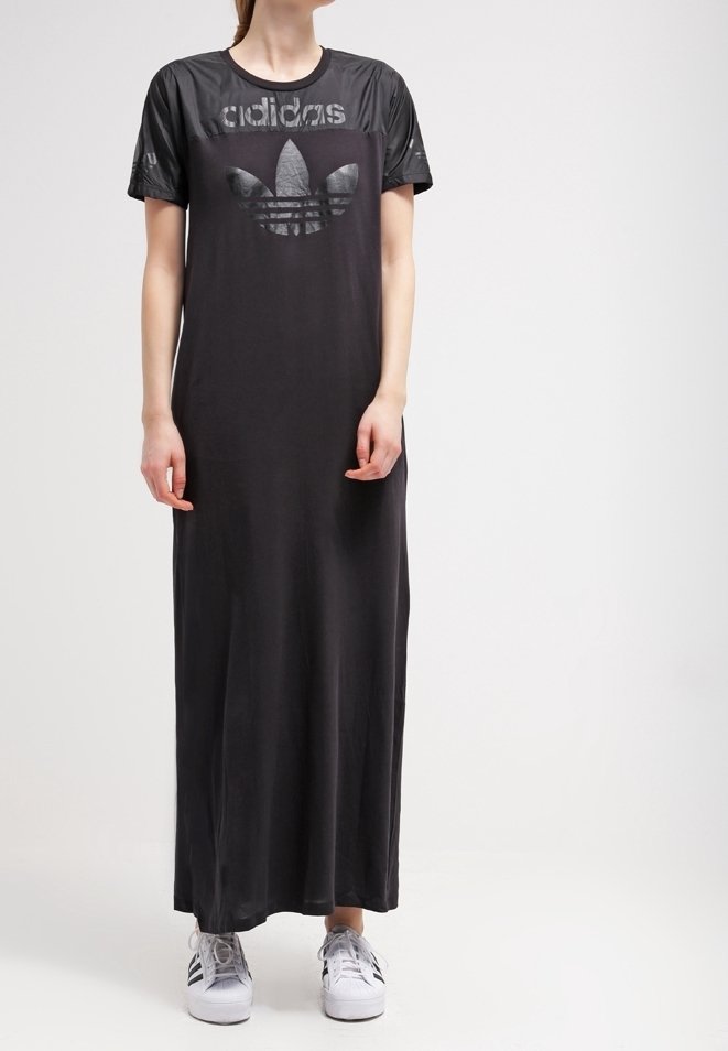 Vestido maxi negro con mangas cortas brillantes y un destacado logo negro de Adidas. Presenta un corte holgado y está hecho de una tela suave. Se lleva con zapatillas blancas.