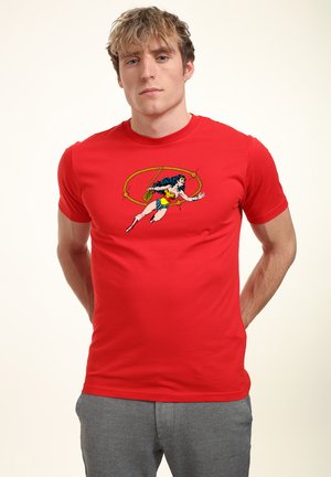 Camiseta roja de manga corta hecha de algodón con un diseño impreso de Wonder Woman en azul, amarillo y blanco, con un detalle de fondo de lazo.