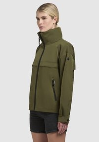 Veste imperméable vert olive avec col montant, fermeture éclair à l'avant et fermeture à bouton-pression, intégrant des poches latérales et des manches courtes avec des accents de boutons.