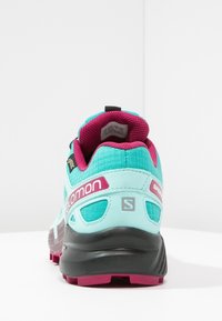 Türkise Sportschuhe mit einem strukturierten Obermaterial, pinken Akzenten und einer stabilen schwarzen Sohle; verfügen über einen gepolsterten Schaft und Logodetails.