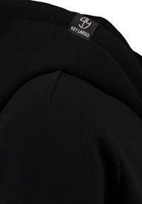 Sudadera negra con tejido de algodón suave, bordes acanalados y una etiqueta con el logo en el cuello. El diseño incluye un ajuste cómodo y relajado.