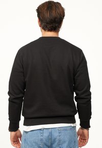Black crewneck sweatshirt in a ribbed texture, fitted cuffs, and hem. Worn over a white shirt, paired with light blue denim shorts.