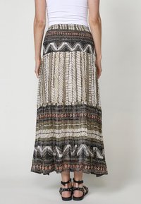 Maxi rok met een gelaagd ontwerp, met zwarte, witte en roestkleurige patronen. Lichtgewicht stof, elastische tailleband en enkellange snit.