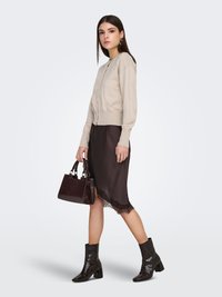 Cardigan en maille beige, robe nuisette en satin noir avec bordure en dentelle, bottines noires texturées, et sac à main marron foncé embossé crocodile.
