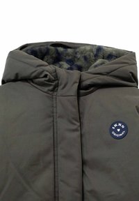 Donkergrijze gewatteerde jas met capuchon, gevoerd met zacht nepbont en een ronde marineblauwe "IKKS Original" patch op de borst.