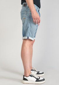 Shorts en denim bleu clair avec des revers, présentant un design classique à cinq poches et une étiquette en cuir sur la ceinture arrière.
