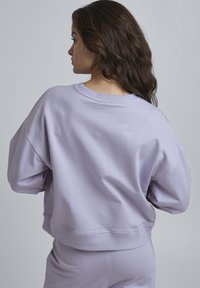 Felpa lavanda con vestibilità comoda, scollatura a girocollo a costine e spalle cadenti. Tessuto liscio, orlo corto e dettagli di cucitura minimi.