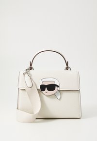 Borsa a mano in pelle bianca texturizzata con manico superiore, dotata di una spilla con personaggio in bianco e nero e di una tracolla rimovibile.