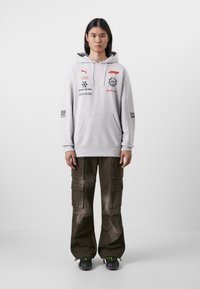 Hanorac gri cu buzunar tip kengur și logo-uri. Asortat cu pantaloni cargo negri, cu multiple buzunare. Adidași cu accente de galben.