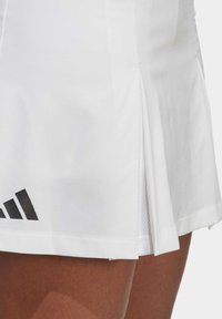 Witte sportrok met een gestructureerde afwerking, voorzien van zijplooien en een zwart Adidas-logo aan de zoom. Glad materiaal en vrouwelijke snit.
