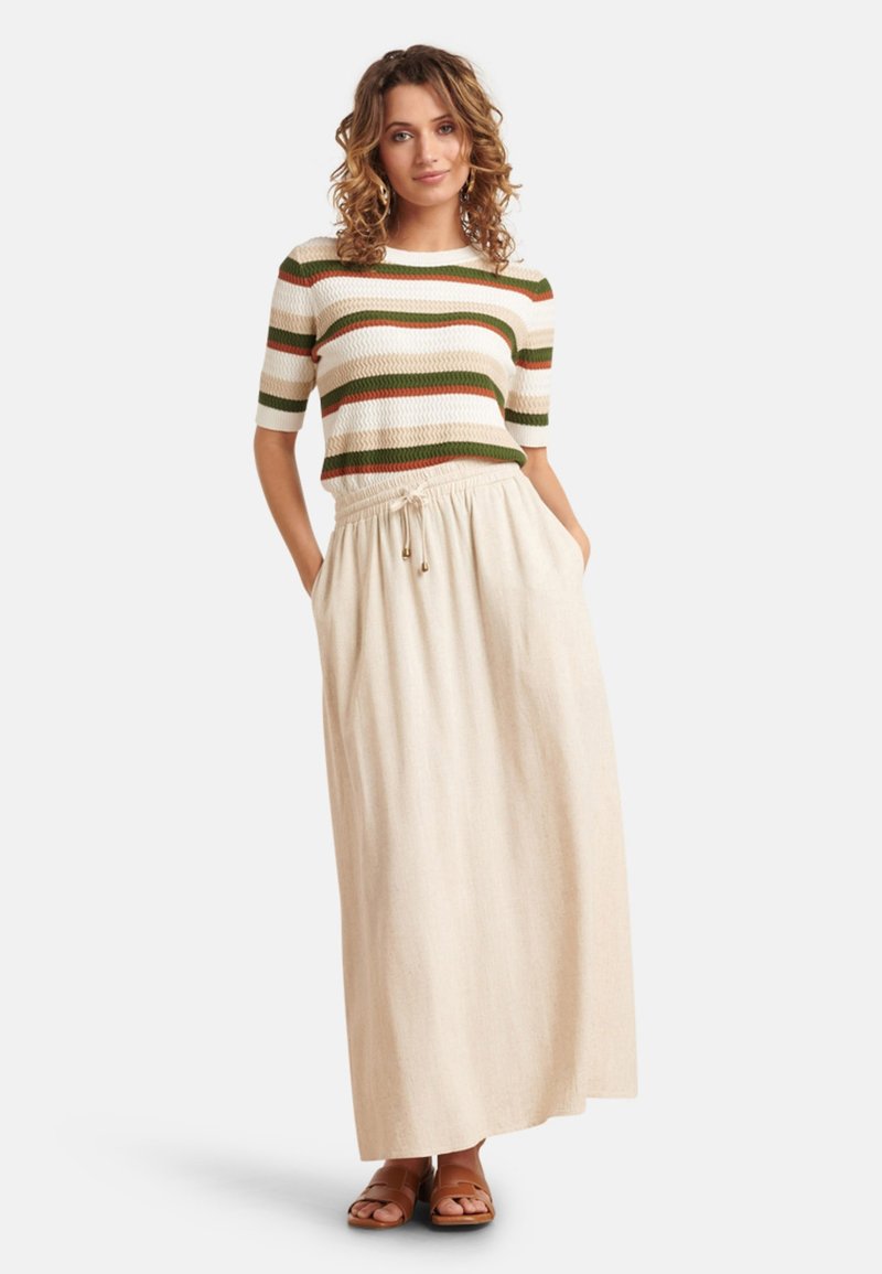 Gebreide gestreepte trui in crème, groen en oranje, gecombineerd met een beige maxi rok met elastische tailleband en zijzakken. Bruine sandalen.