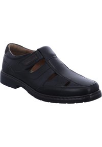 Black leather slip-on shoe featuring cutout panel design, rounded toe, textured stitching, and a cushioned tan interior.