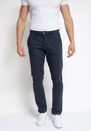 Chinos azul marino de algodón, con cierre de cremallera, bolsillos laterales y un diseño ajustado, combinados con zapatillas blancas.