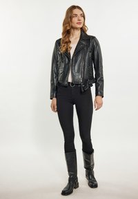 Jachetă de motociclist din piele neagră, cu accente cu țepi, buzunare cu fermoar și un design ajustat. Pur și simplu peste un top ușor, combinată cu pantaloni negri și cizme.