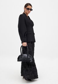 Sort skræddersyet blazer med puffede ærmer, parret med en tekstureret sort nederdel og en lille struktureret sort håndtaske. Accessories inkluderer sorte solbriller.