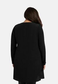 Svart långärmad tunika med rund halsringning, med en rak passform och längre bak. Mjuk tyg med en slät textur.