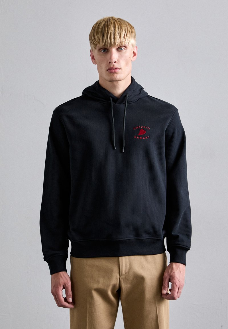Hanorac negru cu glugă, cu textură ribbed, având logo-ul roșu "Emporio Armani" pe piept și șnururi la glugă.