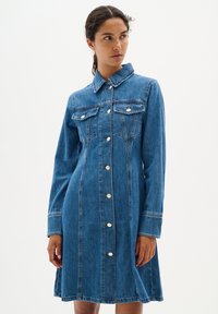 Robe en denim avec col, manches longues, fermeture à boutons sur le devant et deux poches poitrine. Un effet froncé à la taille ajoute une silhouette subtile.