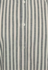 Košela s button-up v svetlosivej a tmavomodrej vertikálnej prúžkovanej textílii, vyrobená z tkaniny s jemnou štruktúrou a so šiestimi bielymi plastovými gombíkmi po celej prednej strane.