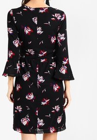 Svart klänning med blommigt mönster i röd, vit och blå. Har utsvängda ärmar och en åtsittande midja, tillverkad av lätt tyg.