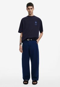 Camiseta navy de gran tamaño con gráfico de palmera, combinada con pantalones anchos navy y sandalias negras. El conjunto presenta un corte relajado.