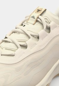Scarpa sportiva beige chiaro con tessuto testurizzato, design a strati e lettering in rilievo. Include una linguetta con il logo.