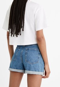 Camiseta blanca de corte corto combinada con shorts de mezclilla azul de tiro alto. Los shorts tienen dobladillos enrollados, dos bolsillos traseros y un corte clásico.